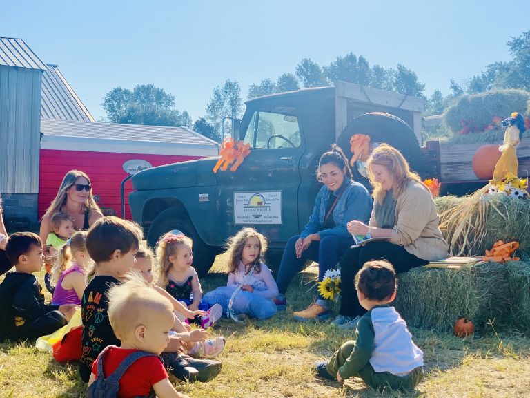 Young children sitting on the grass for a fall farm storytime with Sandhills Friends
